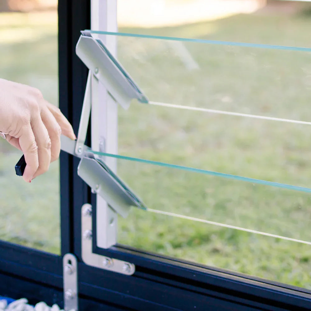 Hand operating glass louvre window with adjustable metal hinges in outdoor setting