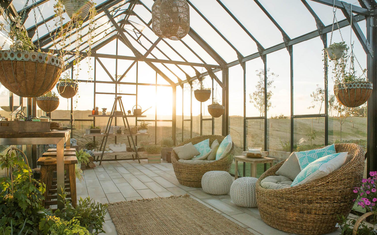 Sunlit modern greenhouse with wicker chairs, hanging plants, wooden table, and garden decor