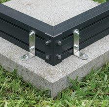 Foundation surface mounting kit securing black metal frame to concrete slab with grass surrounding